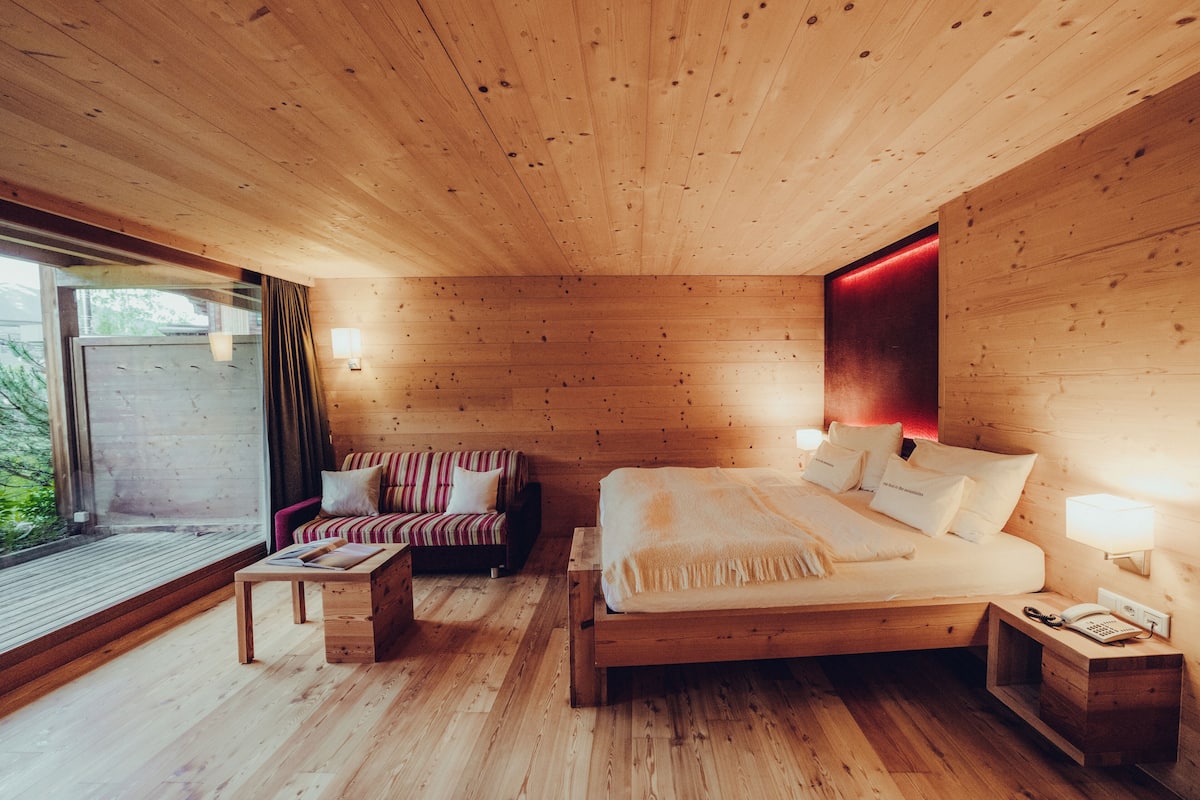 A wooden cabin bedroom with a bed, a sofa, a small table, and a nightstand.