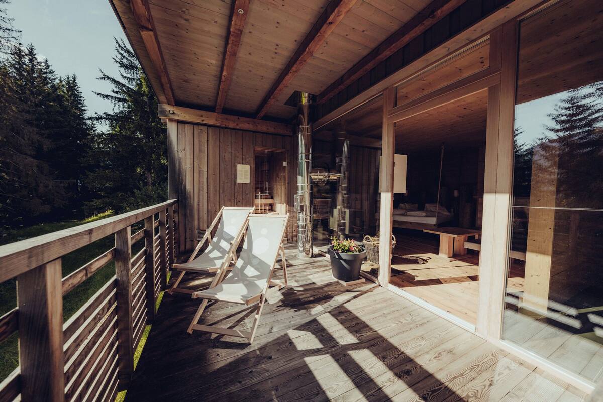 A wooden deck with a glass door leading to a room, a wooden bench, and a potted plant.