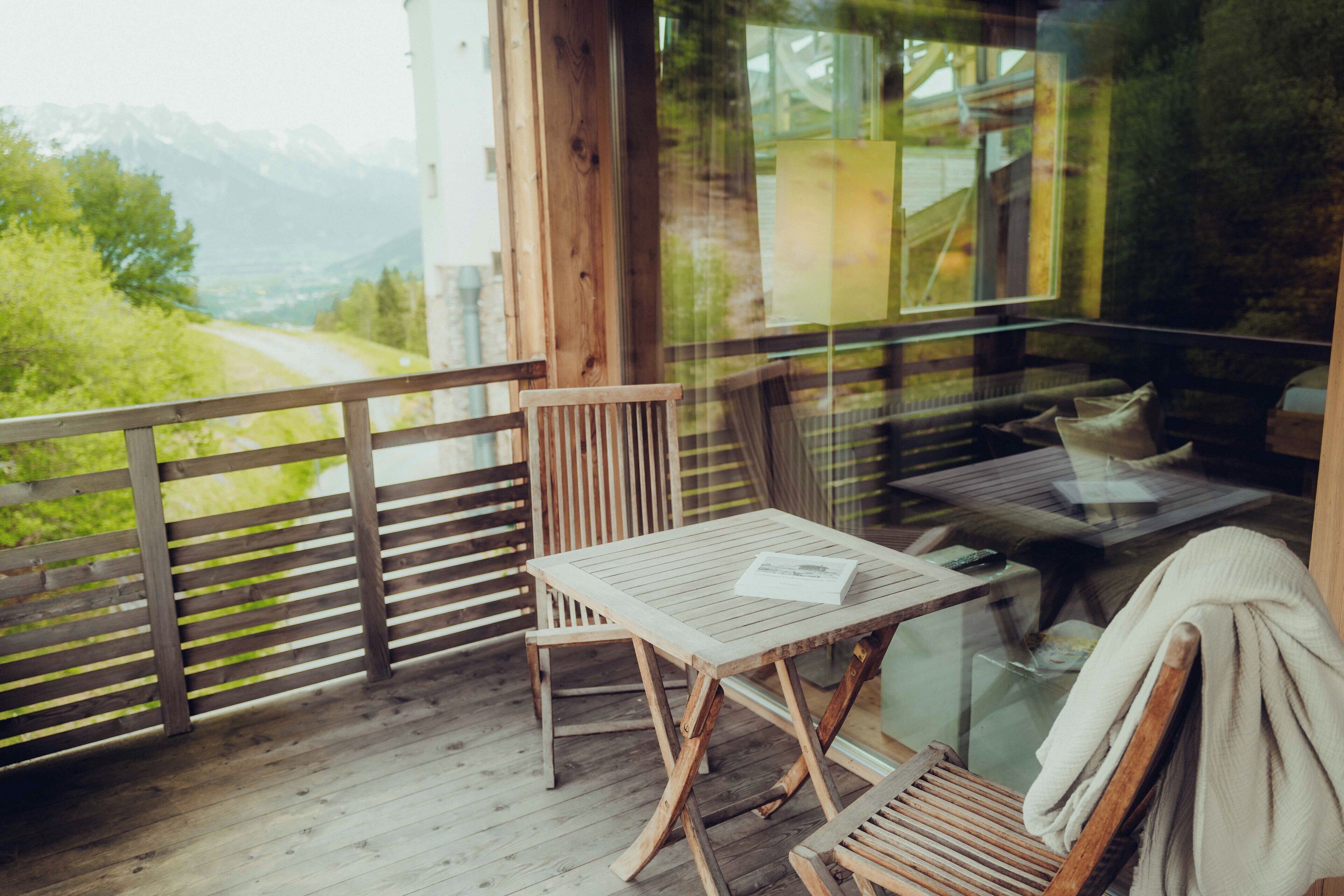 A wooden deck with a table and chairs, a glass door, and a view of a mountain landscape.