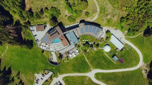 An aerial view of a resort with a swimming pool, sun loungers, and a large building with a curved roof. - Forsthofalm (Leogang)