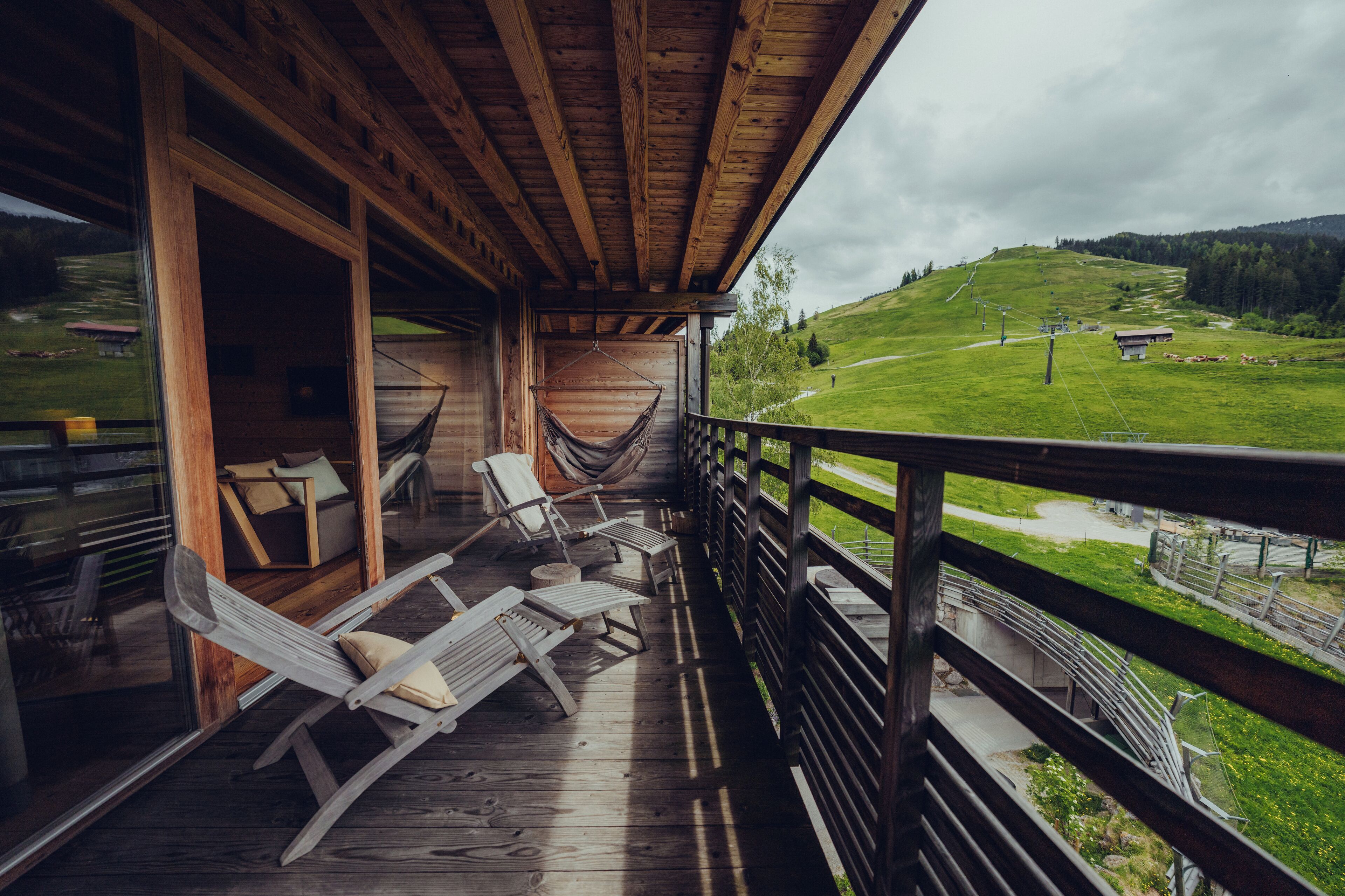 A wooden deck with lounge chairs and a hammock overlooking a green landscape with a ski lift in the distance.