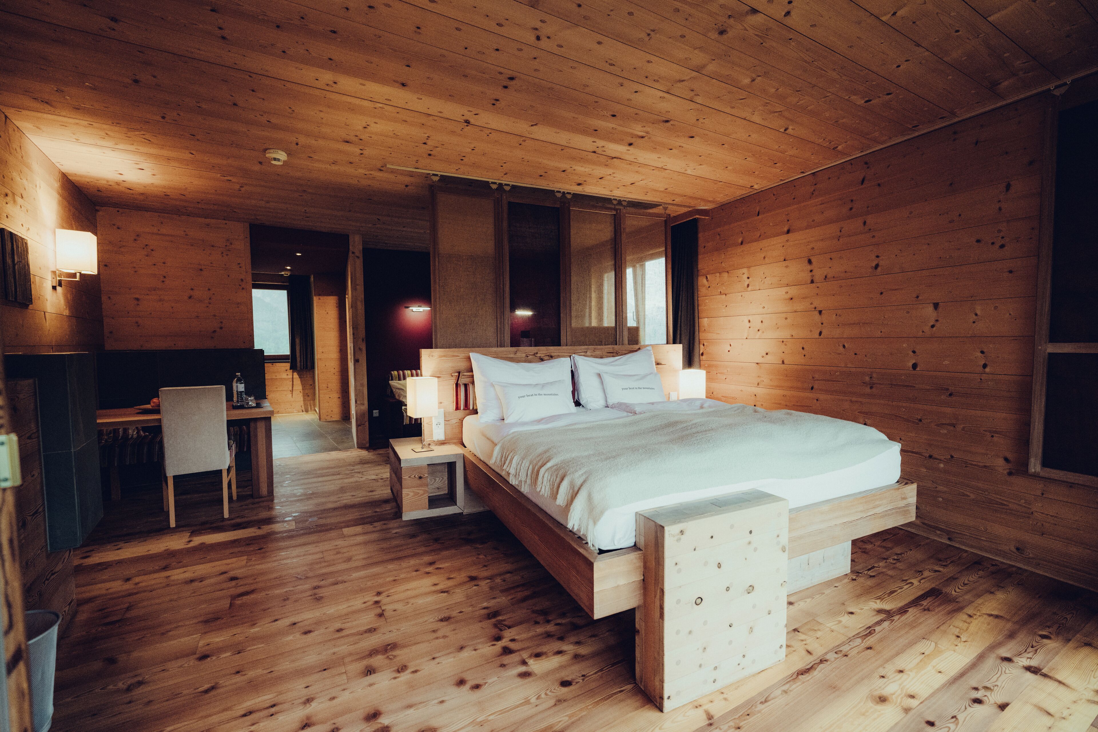 A wooden cabin bedroom with a bed, bedside tables, a desk, and a chair.