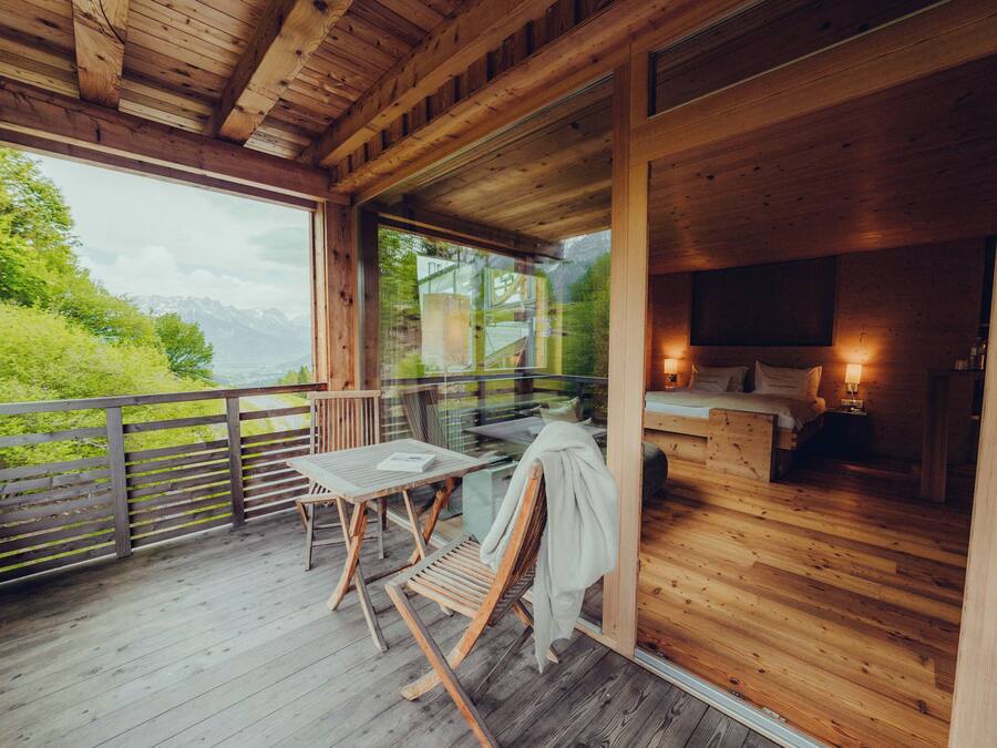 A wooden deck with a table and chairs, a glass door leading to a room with a bed and a TV.
