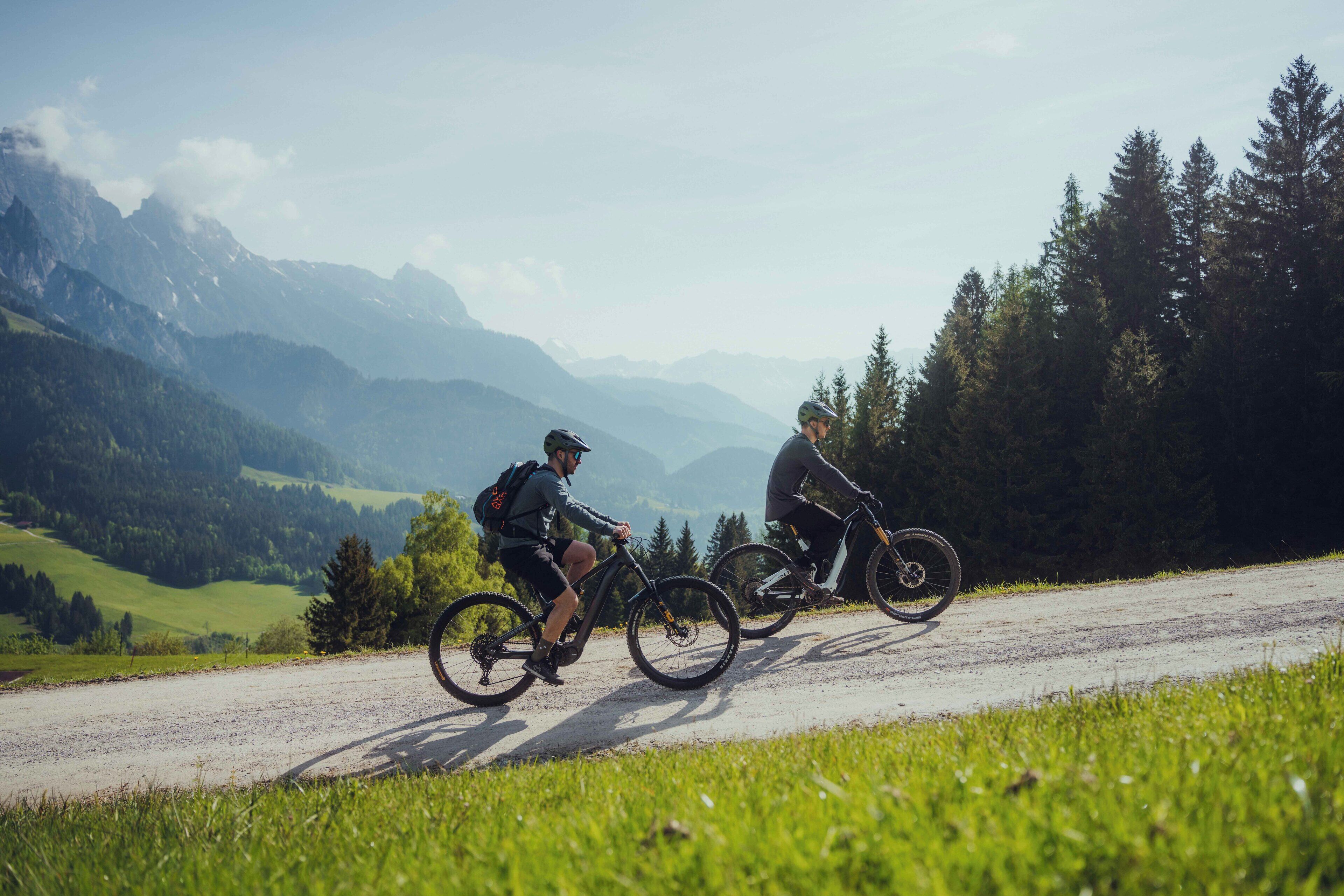Dos ciclistas en un camino de grava con un paisaje montañoso al fondo.