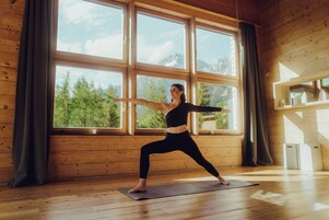 En yogamåtte på gulvet med en person i sort tøj, der udfører en yogastilling foran store vinduer.