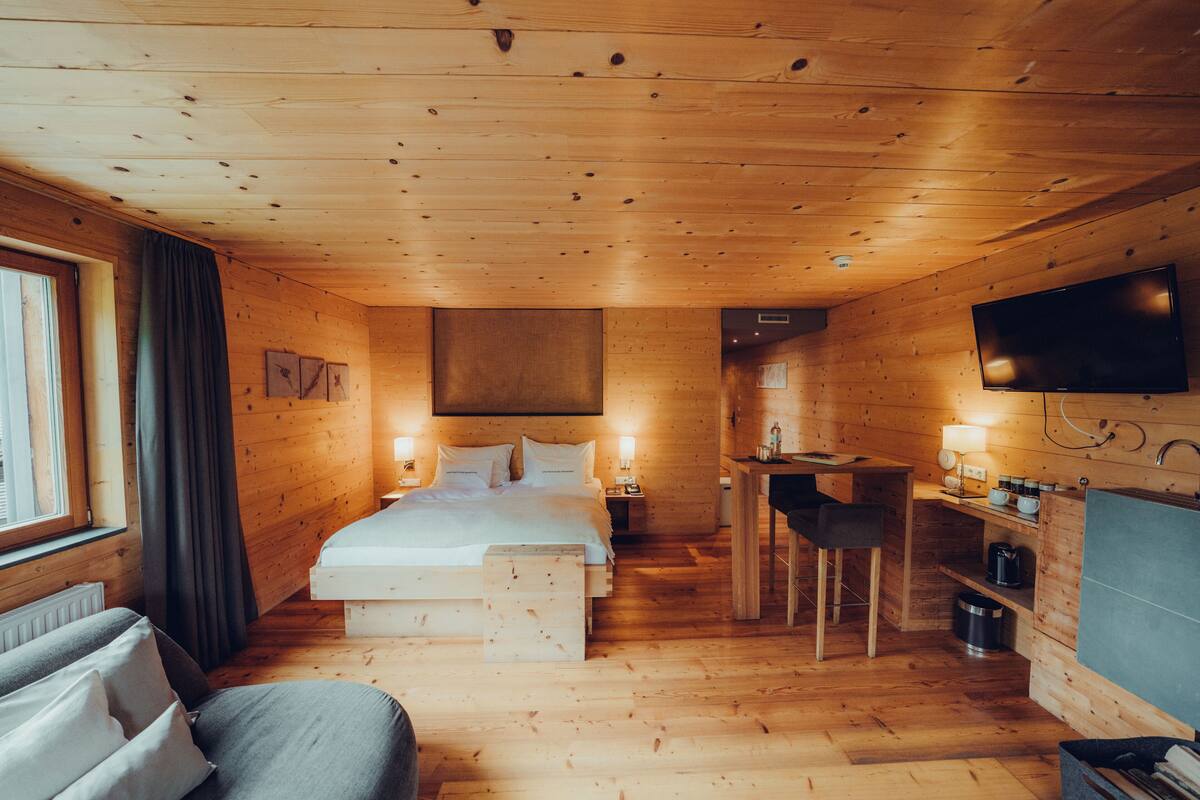 A wooden cabin interior with a bed, a desk, a TV, and a dining area.