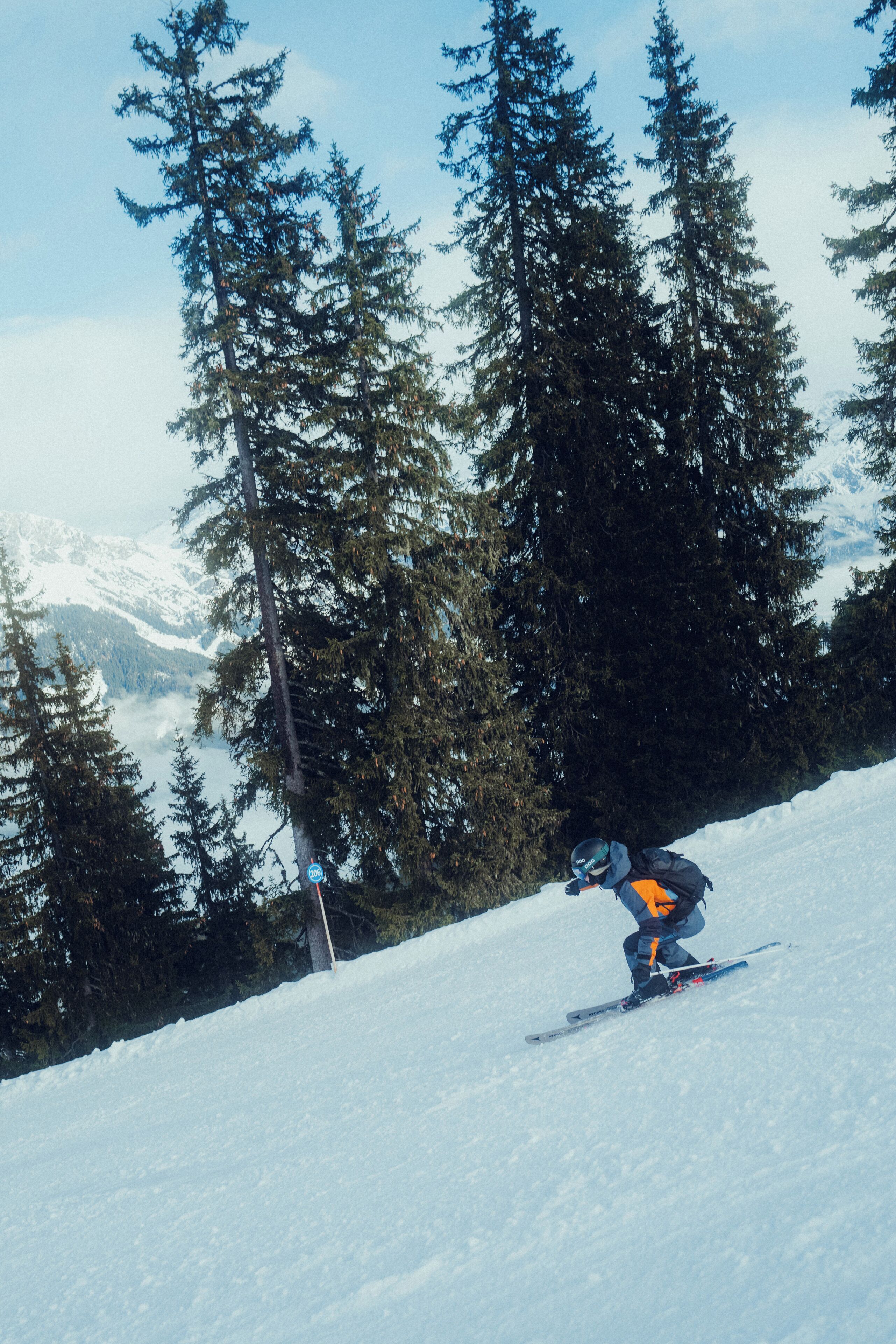 A skier on a snowy slope with tall evergreen trees and distant mountains.