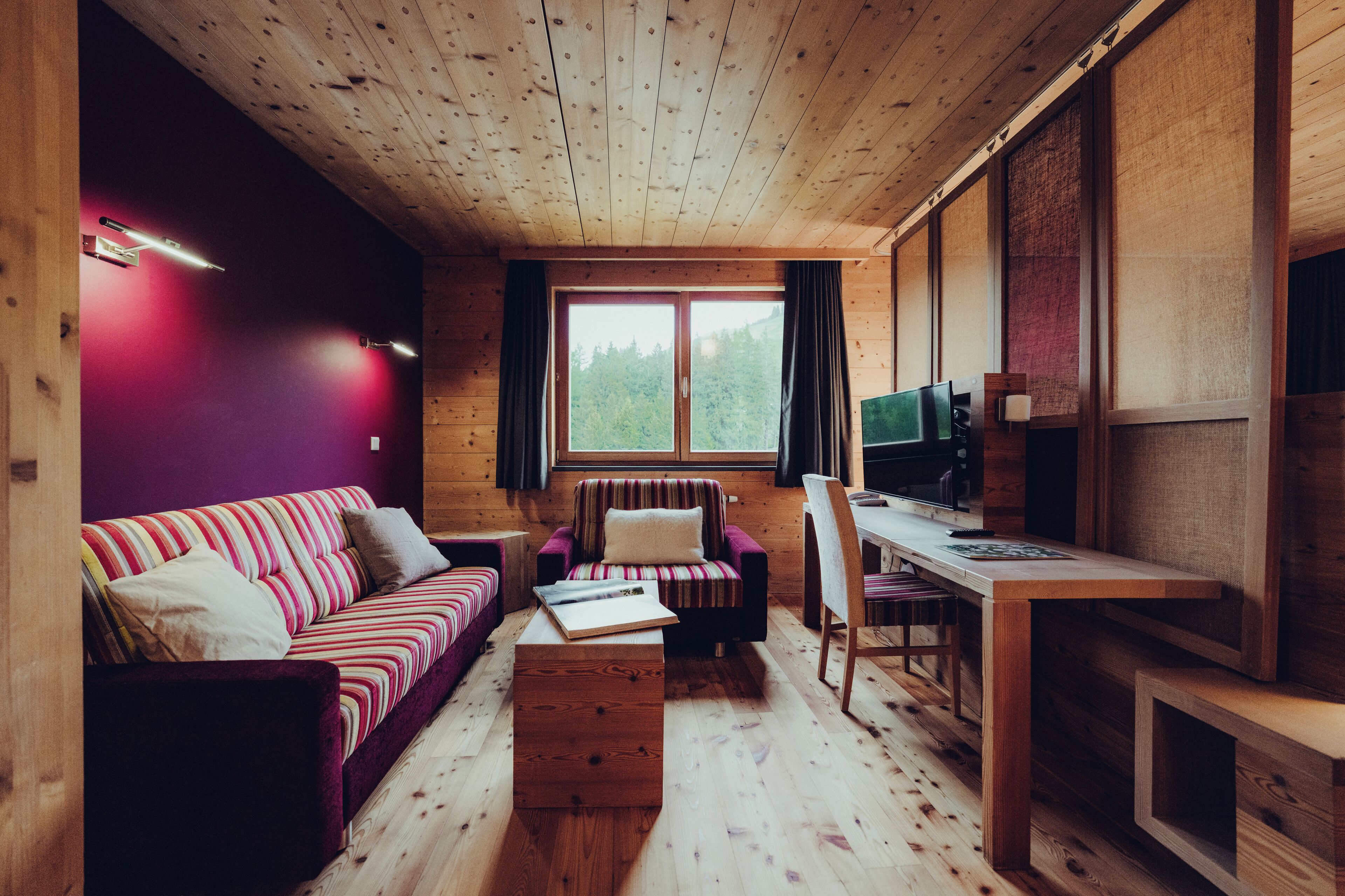 Un interior acogedor de cabaña con techo de madera, un sofá a rayas, un sillón a rayas, una mesa de madera y un televisor.