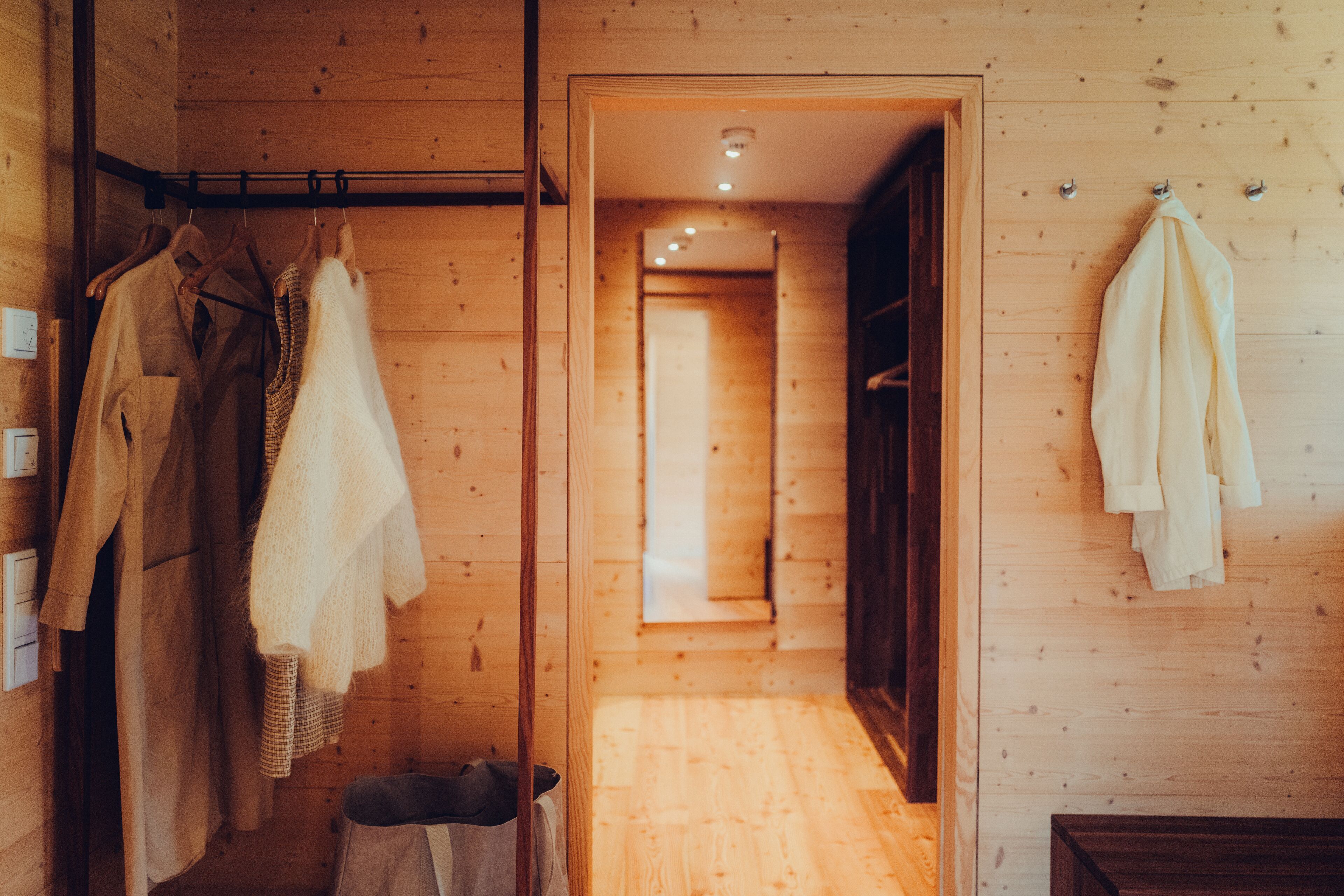 L’intérieur est en bois et un couloir mène à une pièce. Des vêtements sont suspendus sur un portant, et une serviette est posée sur un crochet.