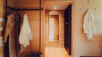 L’intérieur est en bois et un couloir mène à une pièce. Des vêtements sont suspendus sur un portant, et une serviette est posée sur un crochet.