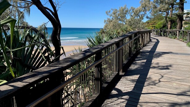 A wooden boardwalk leading to a beach with clear blue water and palm trees. - Coolum Beach Getaway Resort (Coolum Beach)