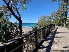 A wooden boardwalk leading to a beach with clear blue water and palm trees.