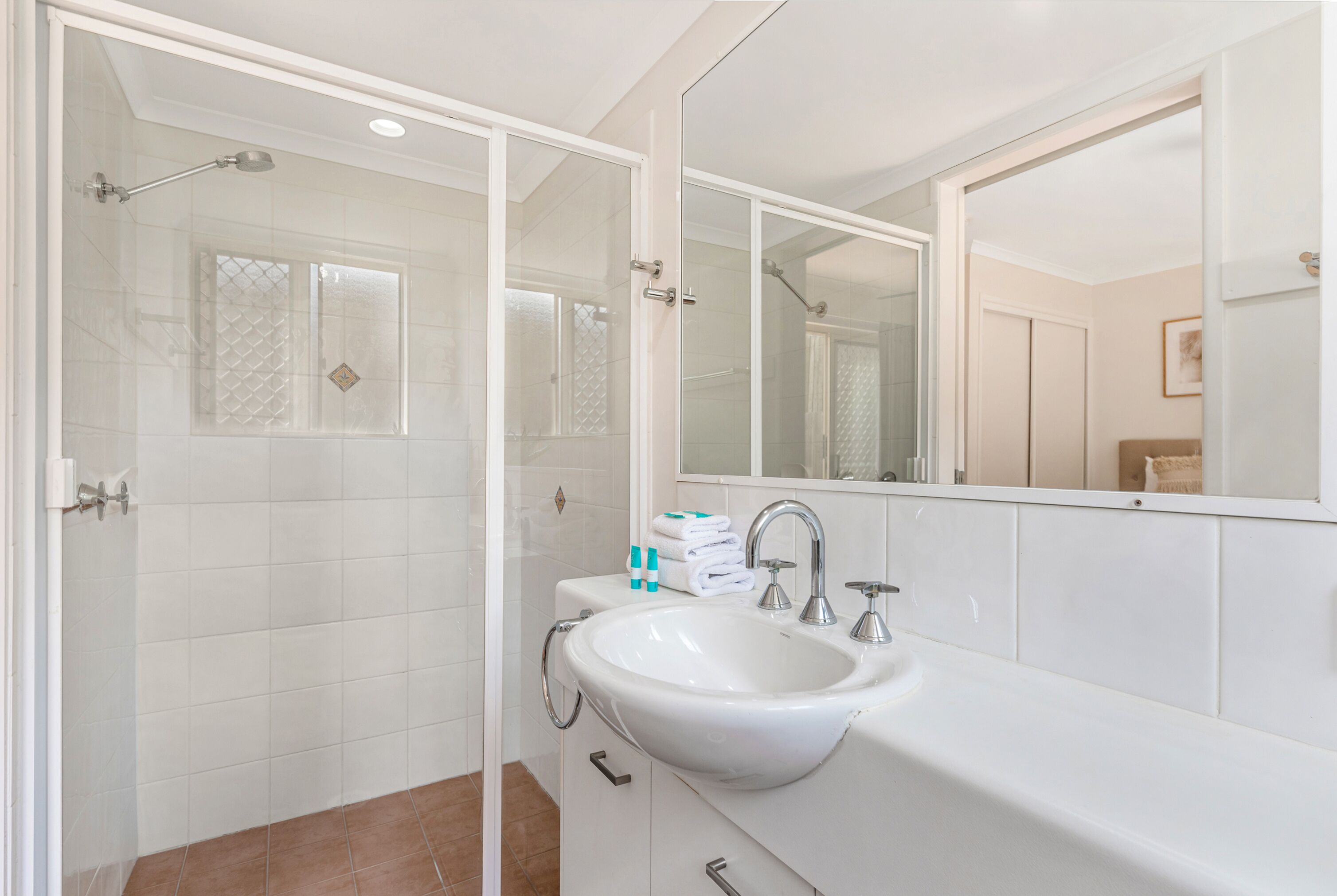 Une salle de bain moderne avec une douche à parois de verre, un lavabo blanc et un grand miroir.