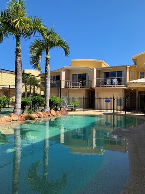 A pool area with clear water, palm trees, and a building with balconies. - Coolum Beach Getaway Resort (Coolum Beach)