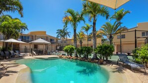 A swimming pool with lounge chairs, palm trees, and a covered seating area. - Coolum Beach Getaway Resort (Coolum Beach)