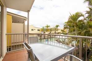 A balcony with a table and chairs, overlooking a tennis court and palm trees. - Coolum Beach Getaway Resort (Coolum Beach)