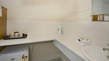 A hotel bathroom with a white sink, a mirror, and a coffee maker on the countertop.