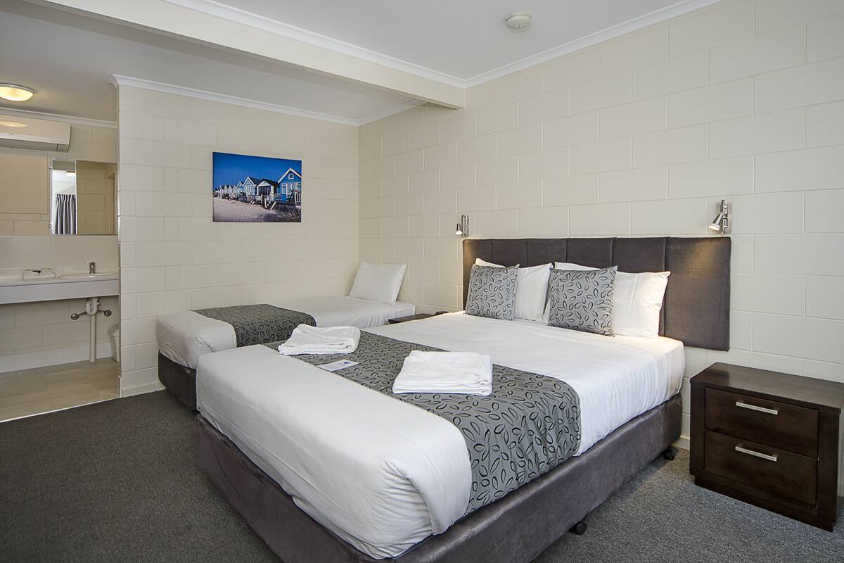 Quarto de hotel com duas camas, um banheiro e uma mesa de cabeceira.
