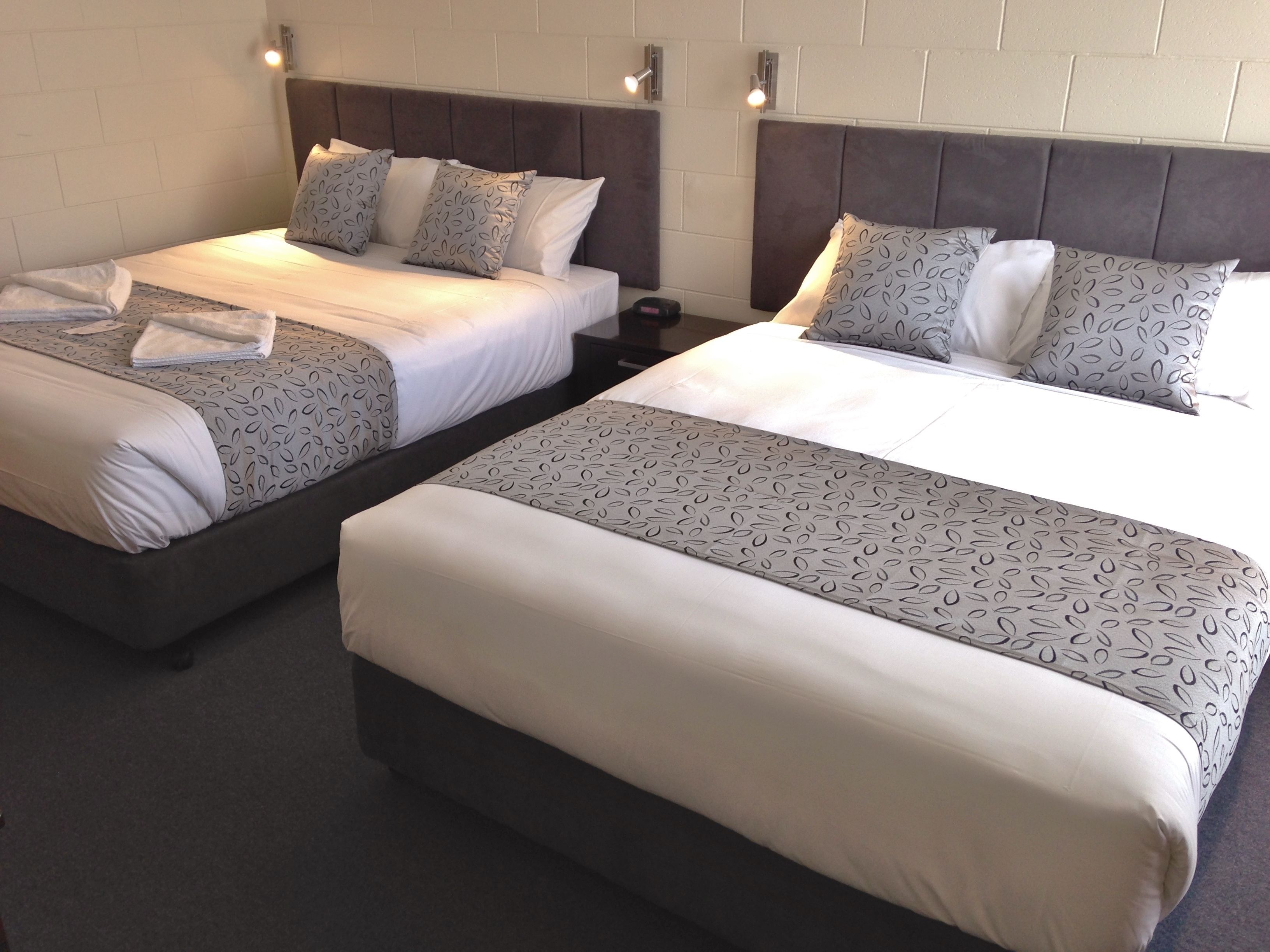 Deux lits jumeaux avec des têtes de lit, du linge de lit blanc et des coussins décoratifs à motifs.