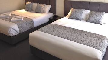 Deux lits jumeaux avec des têtes de lit, du linge de lit blanc et des coussins décoratifs à motifs.