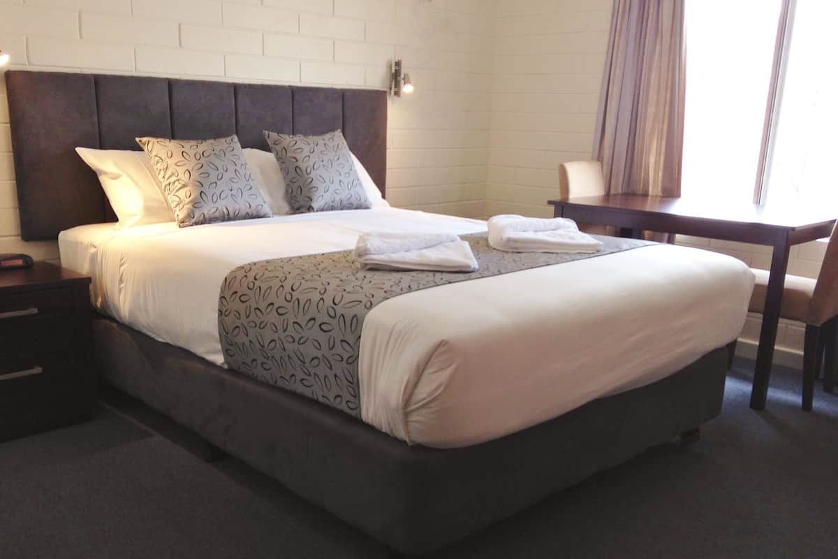 Quarto de hotel com uma cama grande, mesa de cabeceira, escrivaninha e uma cadeira.