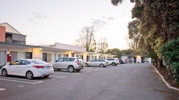 A row of parked cars in front of a motel with a single-story structure and a balcony on the left.