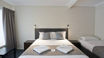 A hotel room with a large bed, two bedside tables, a window with curtains, and a brick-patterned wall.