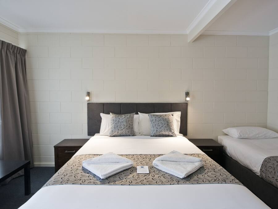 A hotel room with a large bed, two bedside tables, a window with curtains, and a brick-patterned wall.