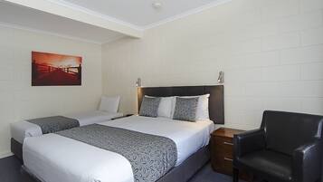 Habitación de hotel con dos camas, una mesita de noche, una silla y un cuadro en la pared.