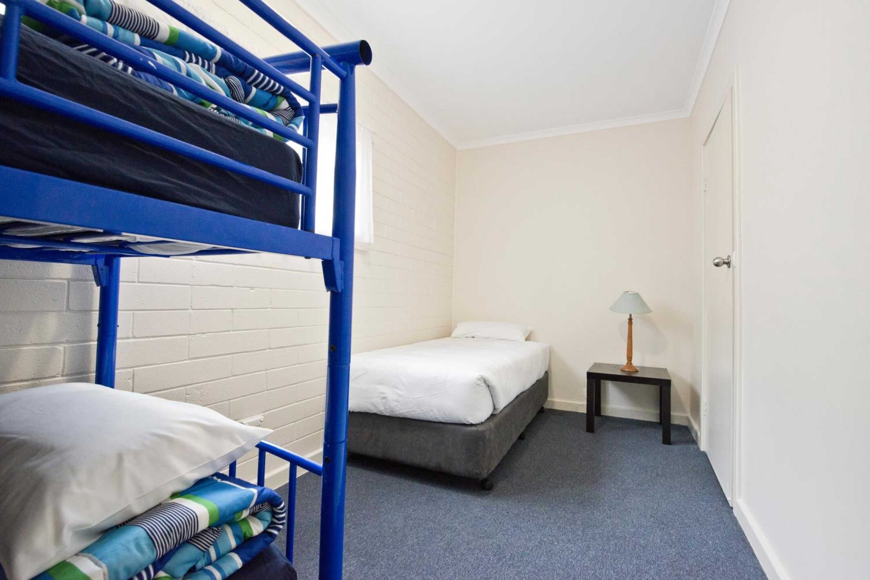 Un dormitorio con literas, una cama individual, una mesita con lámpara y una puerta.