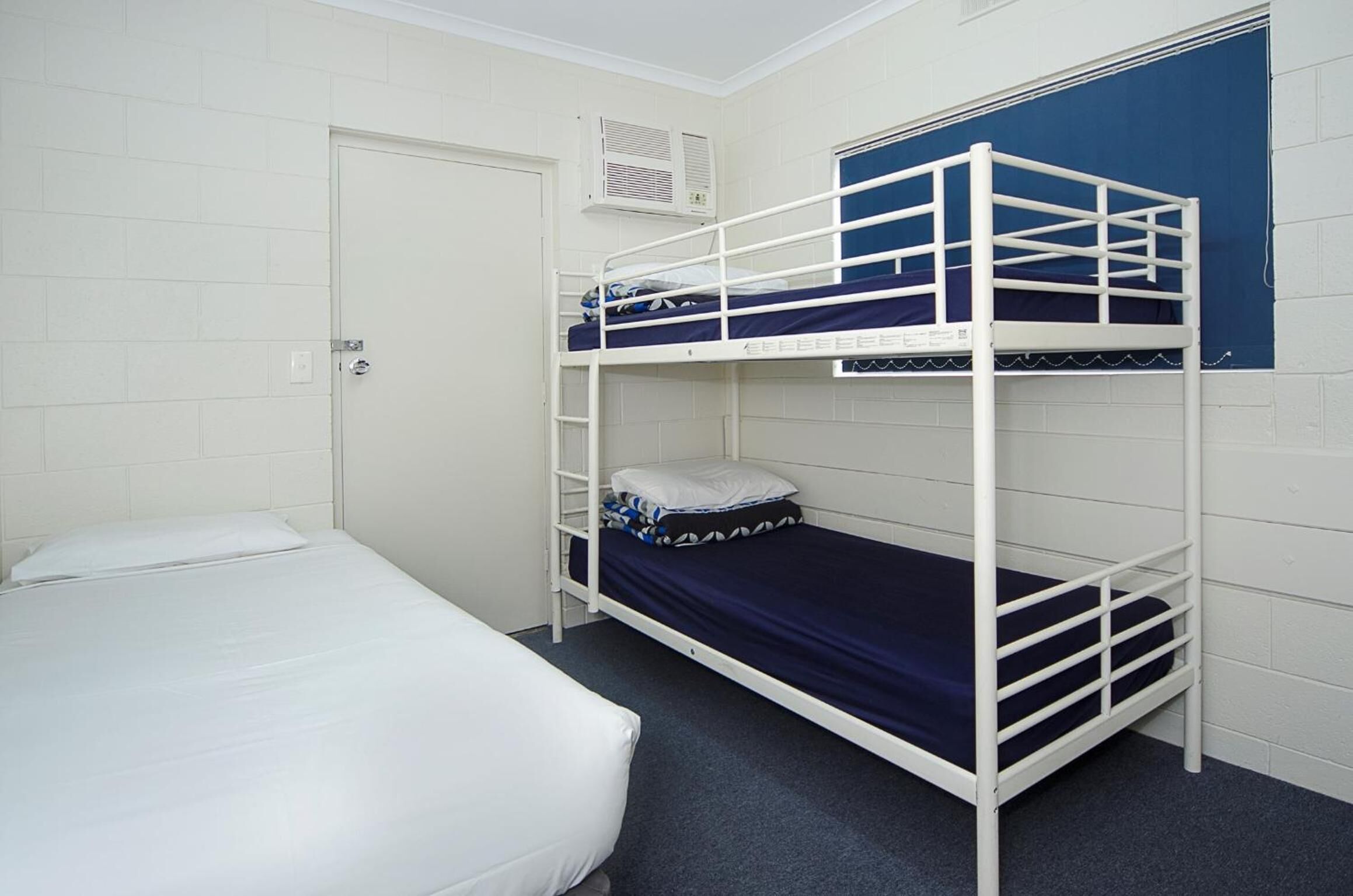 A bunk bed room with a white door, a white air conditioning unit, and a blue curtain.