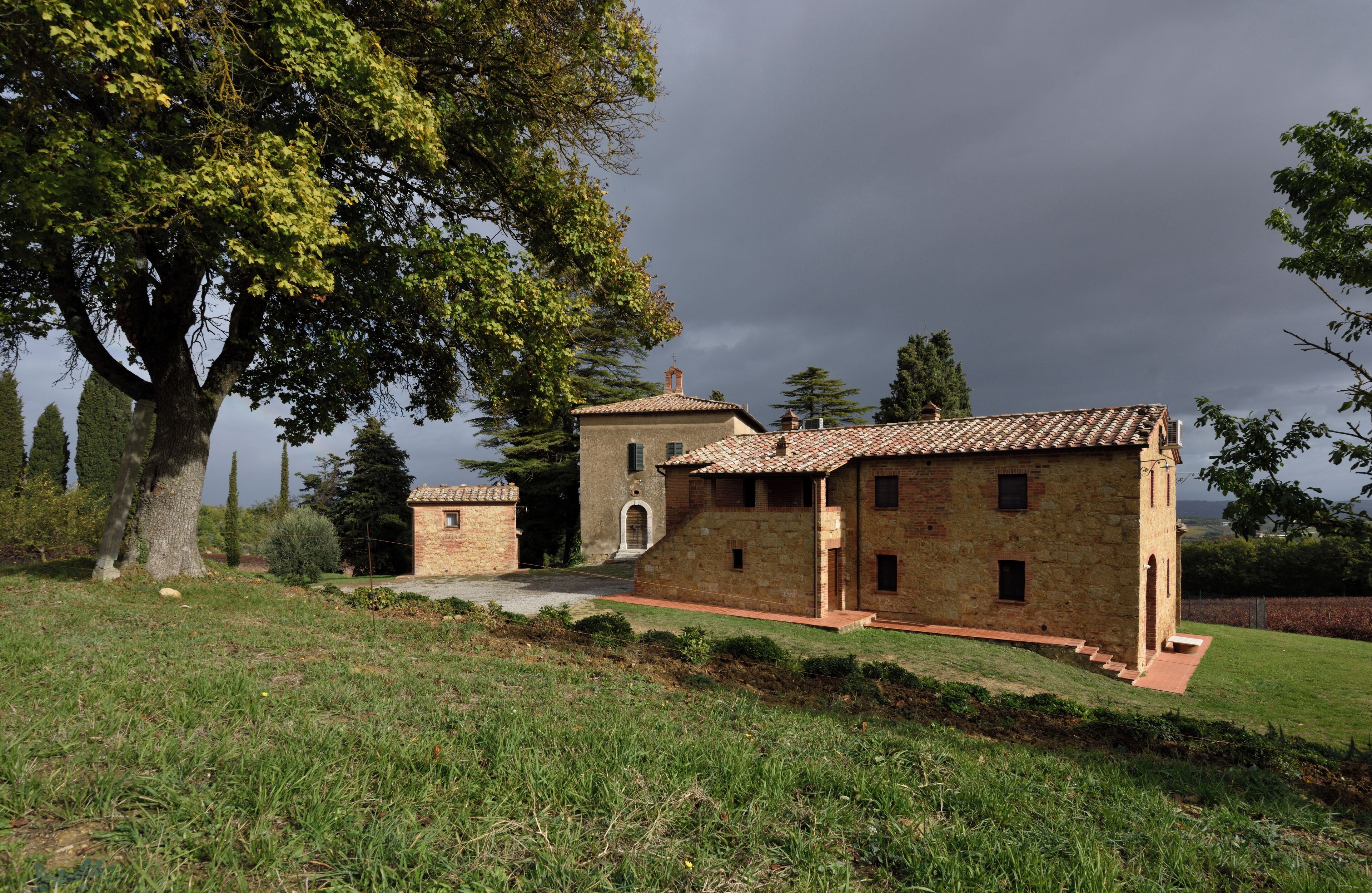 A stone building with a tiled roof, surrounded by grass and trees.