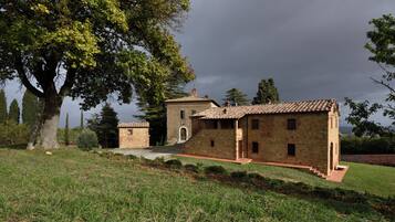 A stone building with a tiled roof, surrounded by grass and trees.
