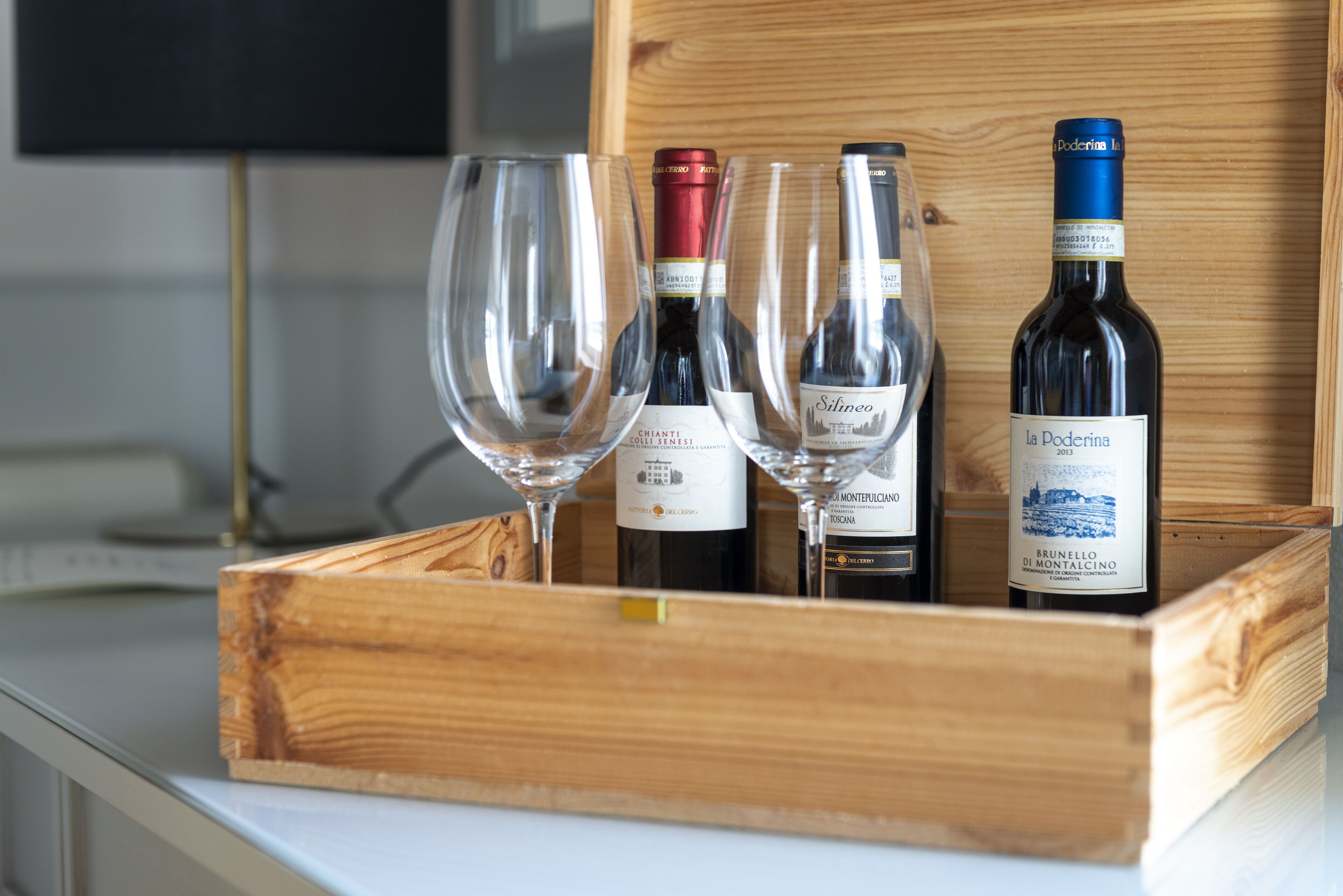 A wooden wine box containing three wine bottles and two wine glasses.