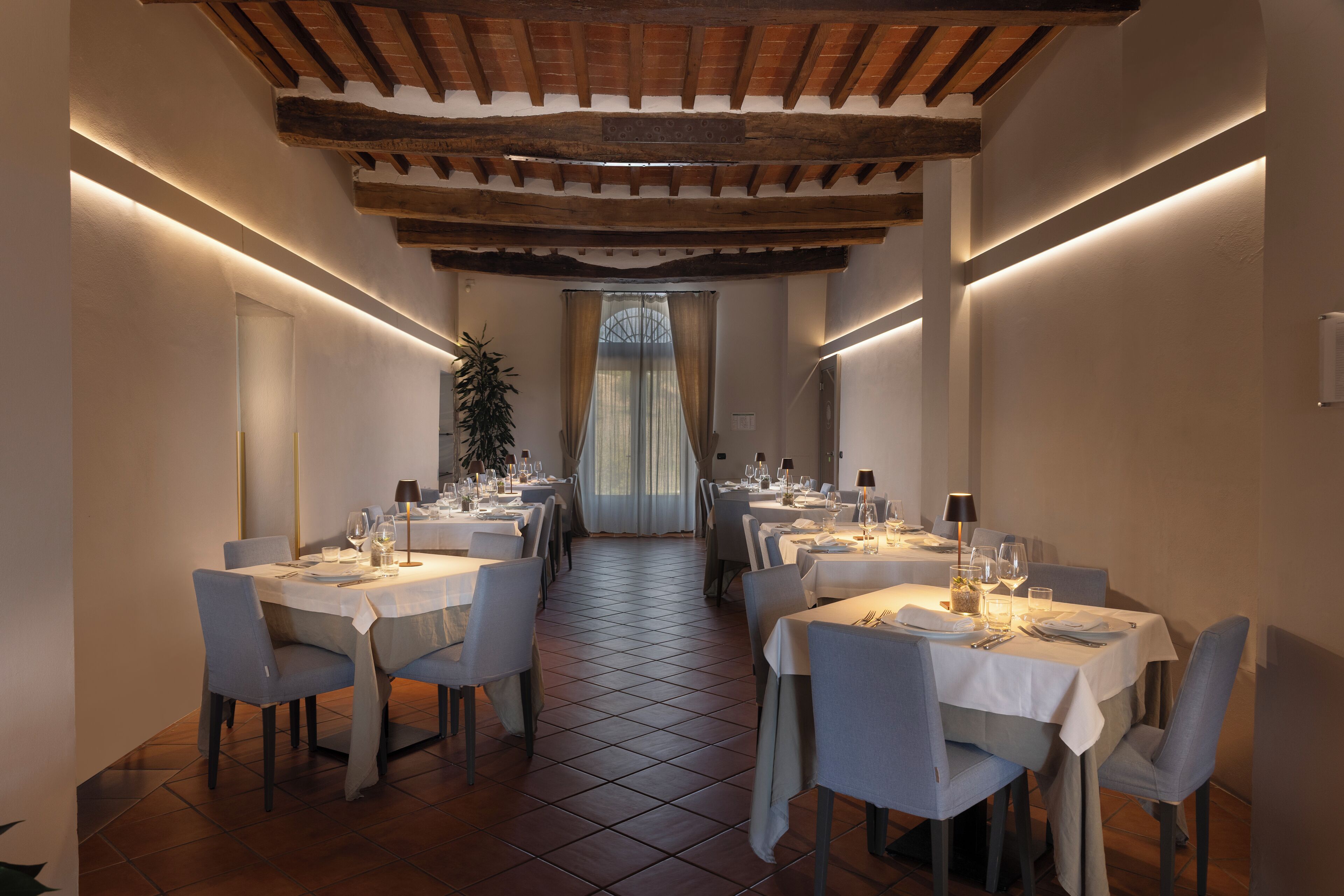 A restaurant with a long table layout, white tablecloths, and modern lighting.