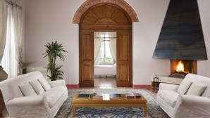 A living room with a fireplace, a sofa, a coffee table, and a view of a bedroom through an arched doorway. - Relais Villa Grazianella - UNA Esperienze (Montepulciano)