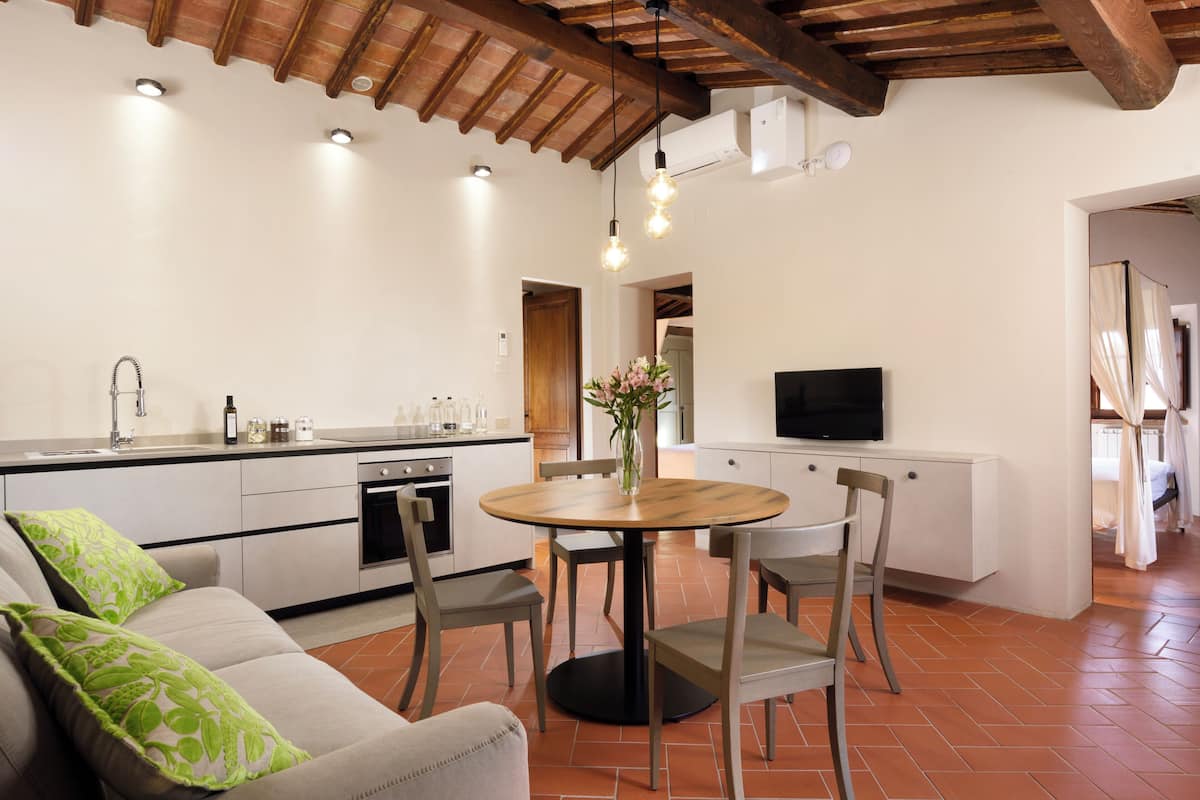 A modern kitchen with a dining area, including a sofa with green pillows, a round wooden table, and chairs.