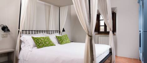A four-poster bed with white and green pillows, a bedside table, and a window with curtains.
