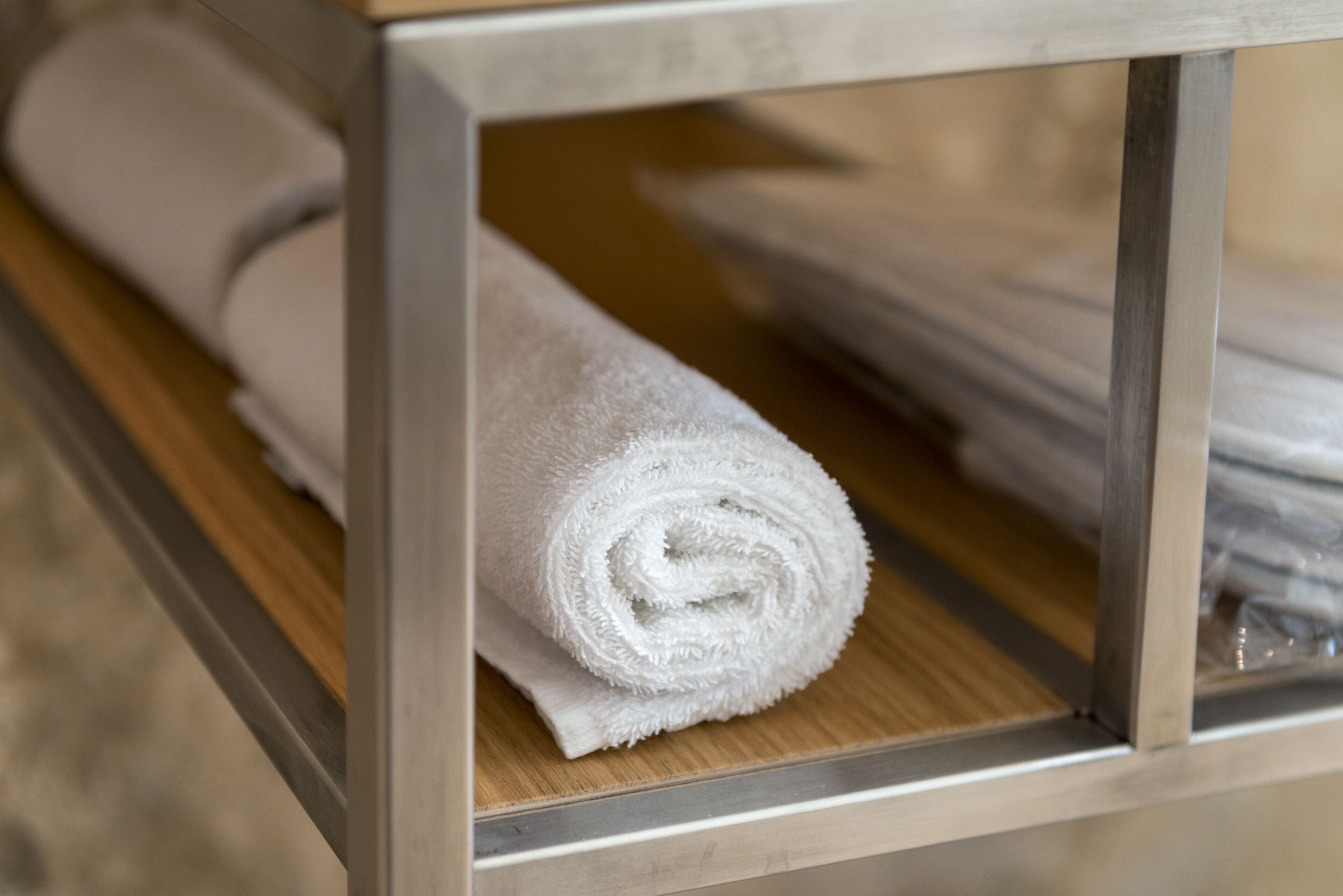 Une serviette blanche enroulée, posée sur une surface en bois à l’intérieur d’une vitrine à cadre métallique.