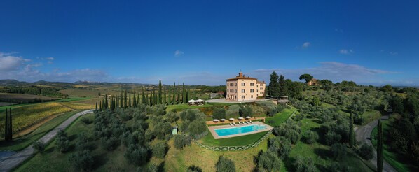 A villa with a swimming pool surrounded by olive groves and a clear blue sky.