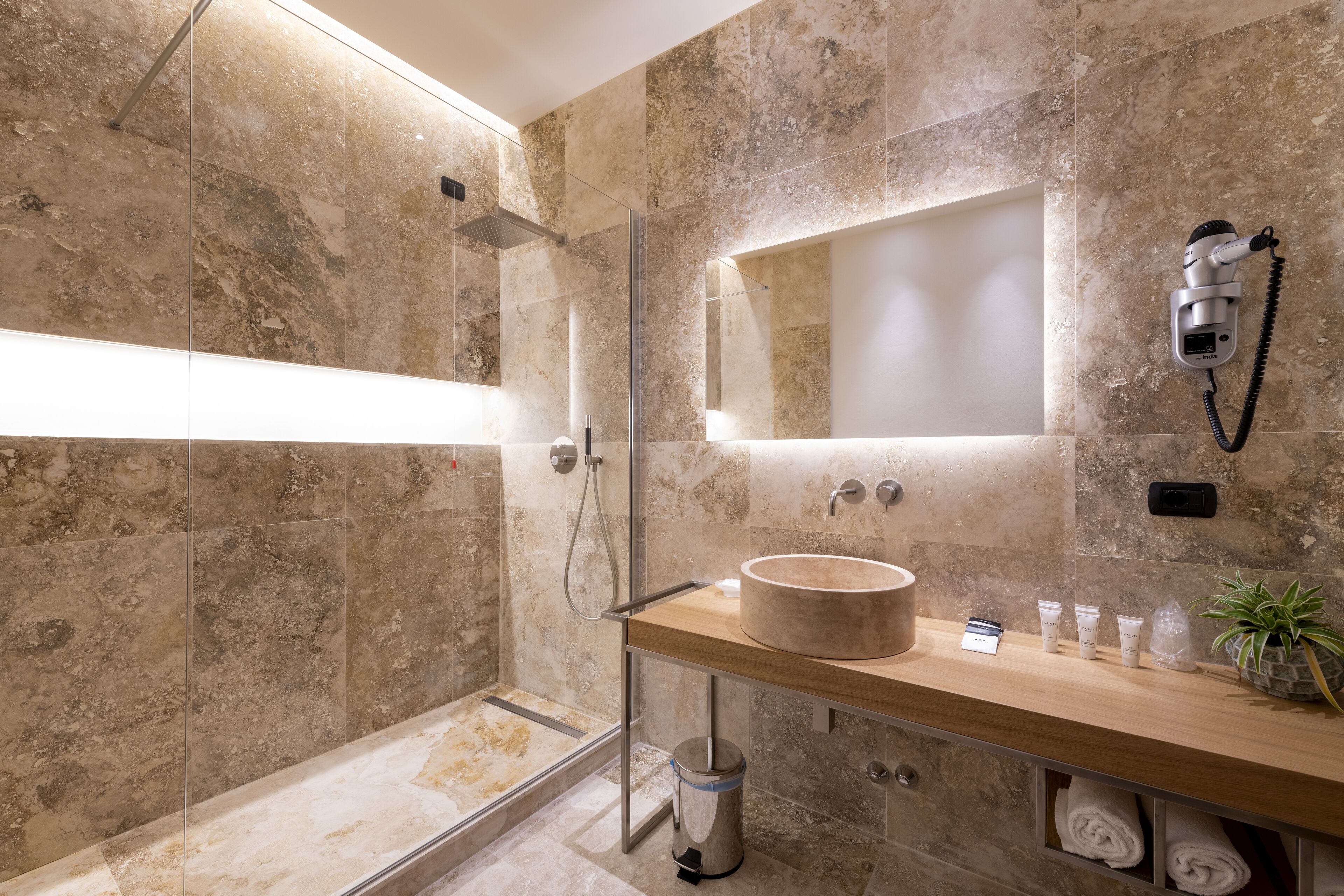 A modern bathroom with a glass-enclosed shower, a wooden vanity with a round sink, and a mounted hairdryer.