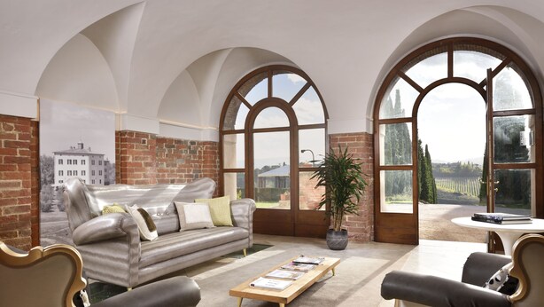 A spacious living room with a leather sofa, a wooden coffee table, and a view through large arched windows. - Relais Villa Grazianella - UNA Esperienze (Montepulciano)