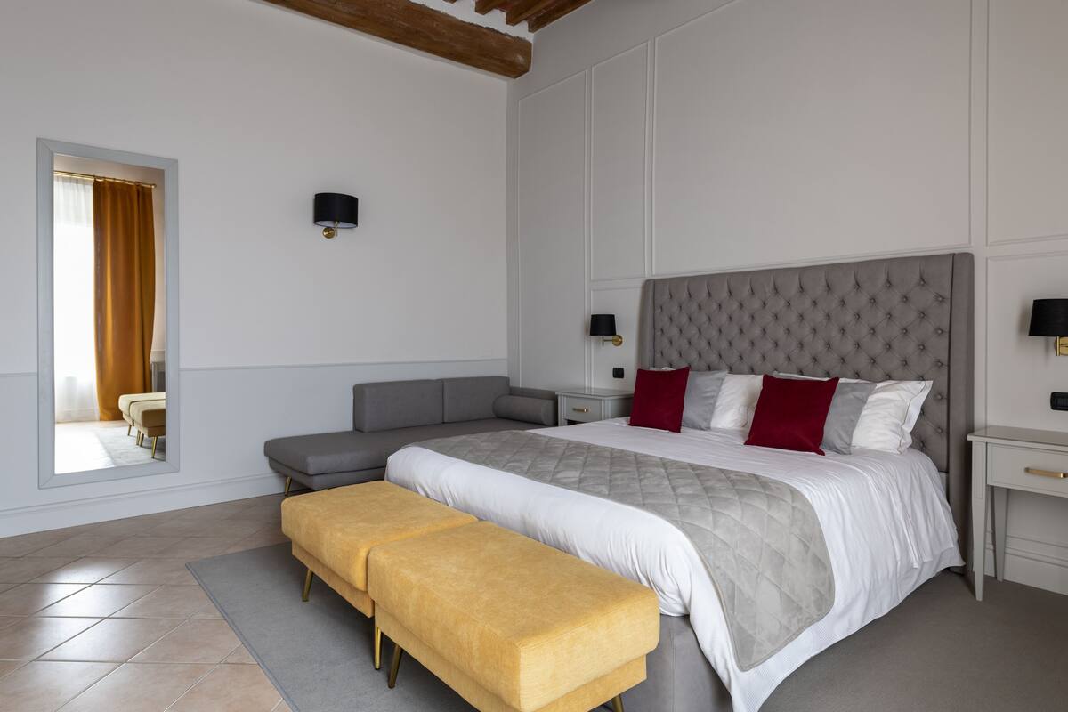 A bedroom with a large bed, a bench, a nightstand, and a mirror.