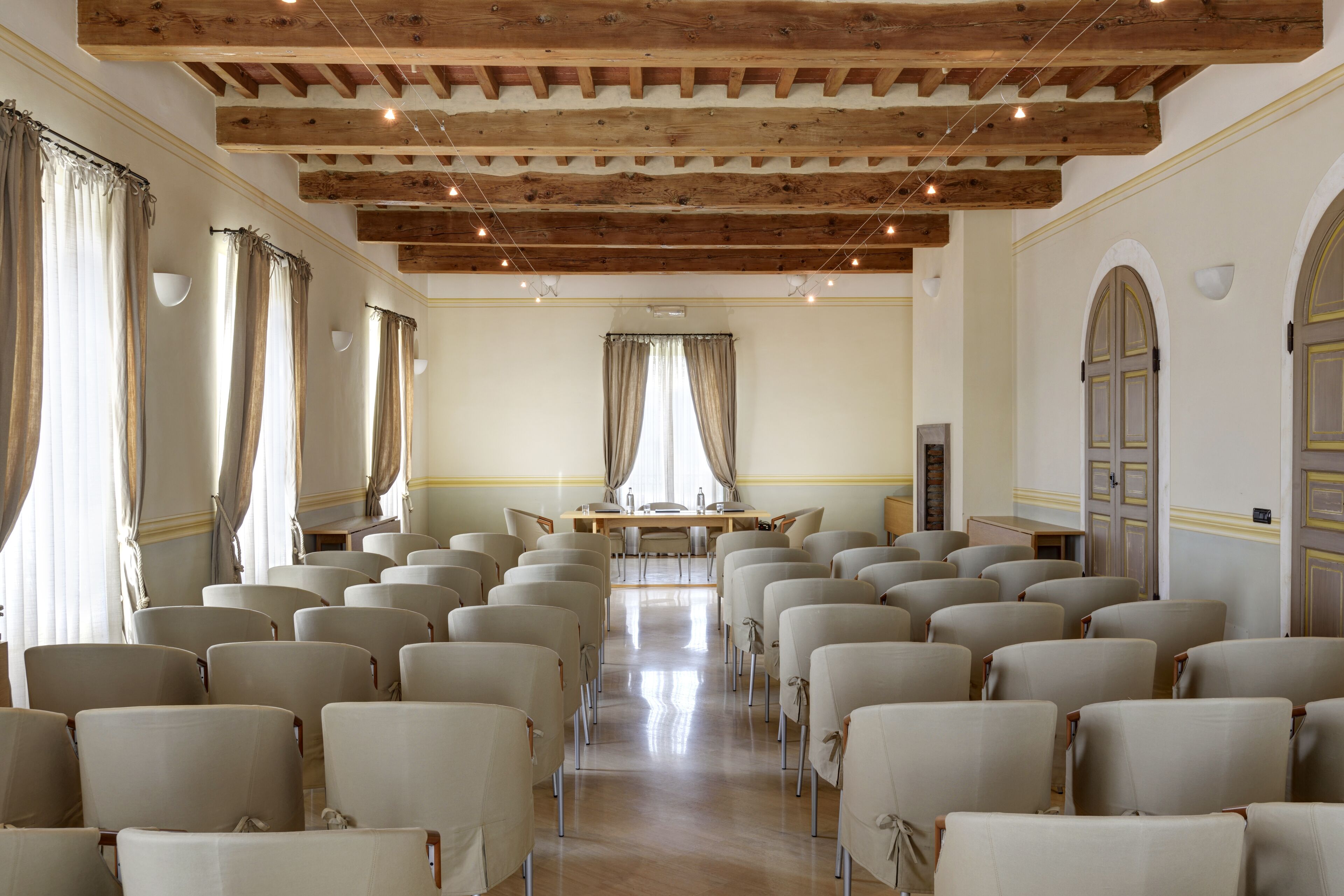 Un salón de conferencias con filas de sillas, techo de madera y ventanas grandes con cortinas.