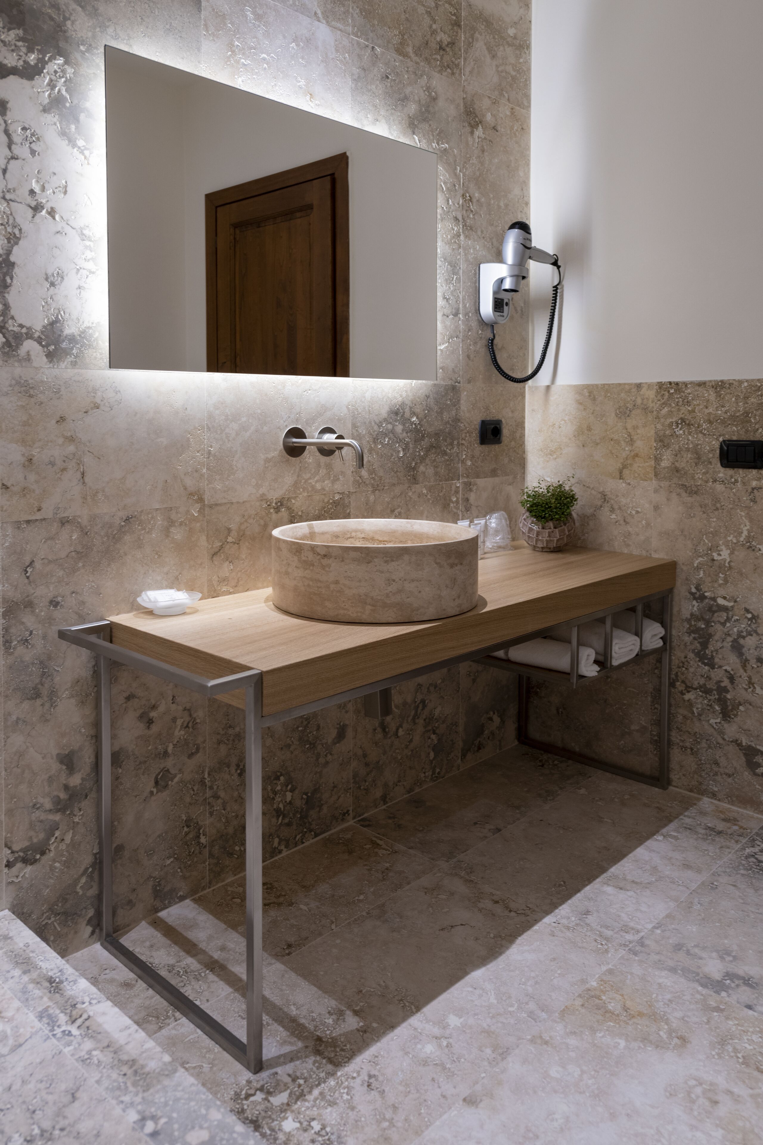 Une salle de bain avec un lavabo en pierre, un meuble-lavabo en bois, un miroir, un porte-serviettes et une petite plante.