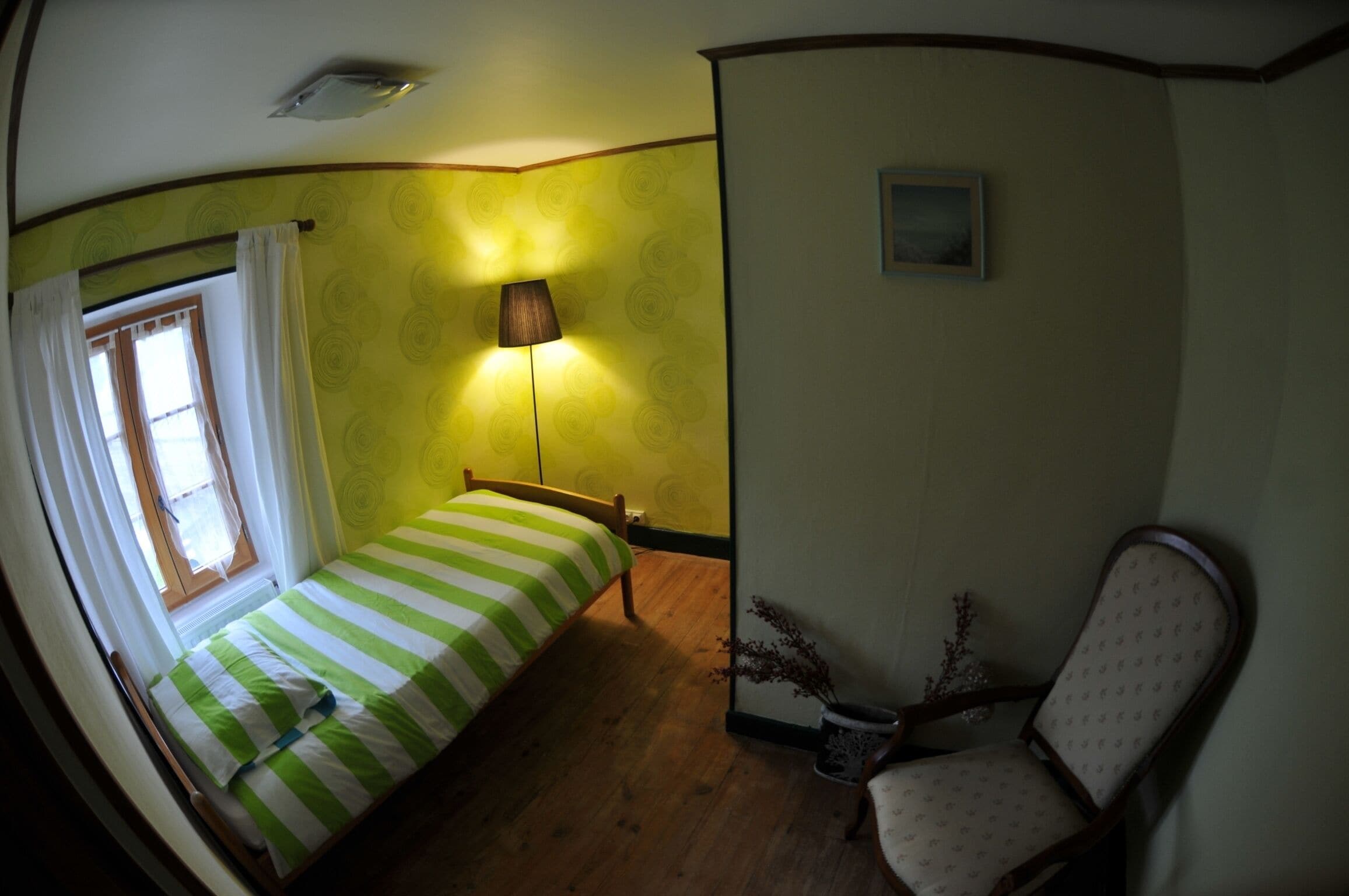 A room with a bed, a chair, a lamp, and a window with curtains.