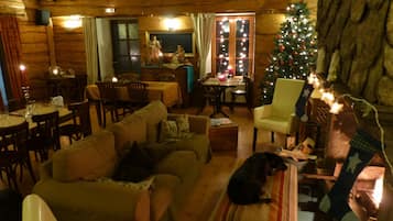 Hyggelig interiør i en træhytte med spiseplads, en stue med sofa og en hund, samt et pyntet juletræ.