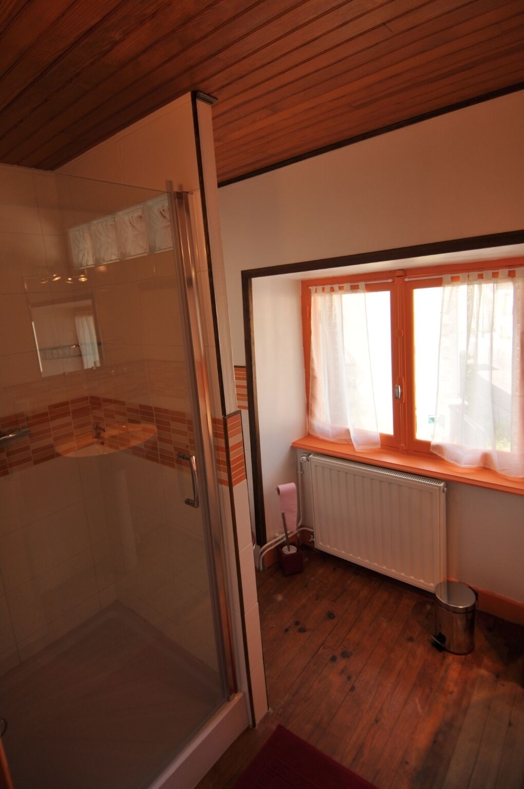 Un baño con cabina de ducha de vidrio, una ventana con cortinas y un radiador.