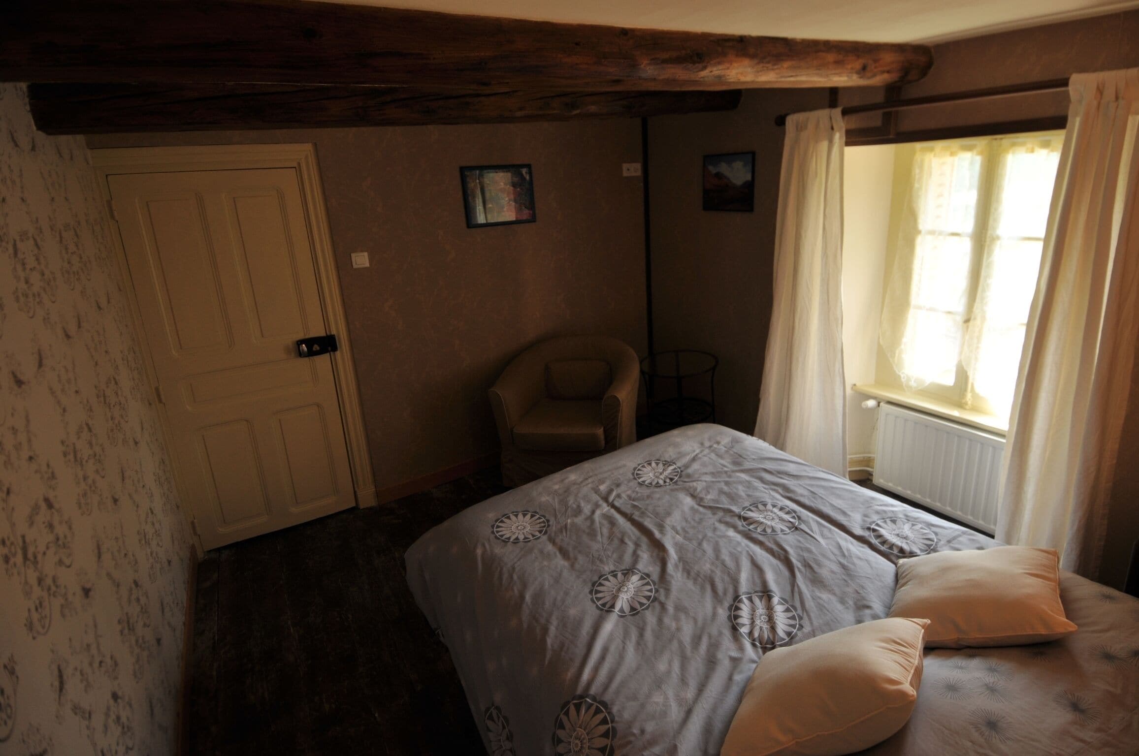 Un dormitorio con una cama, una silla, una puerta y una ventana con cortinas.