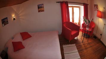 A room with a bed, a red armchair, a small table with a vase, and a lamp.